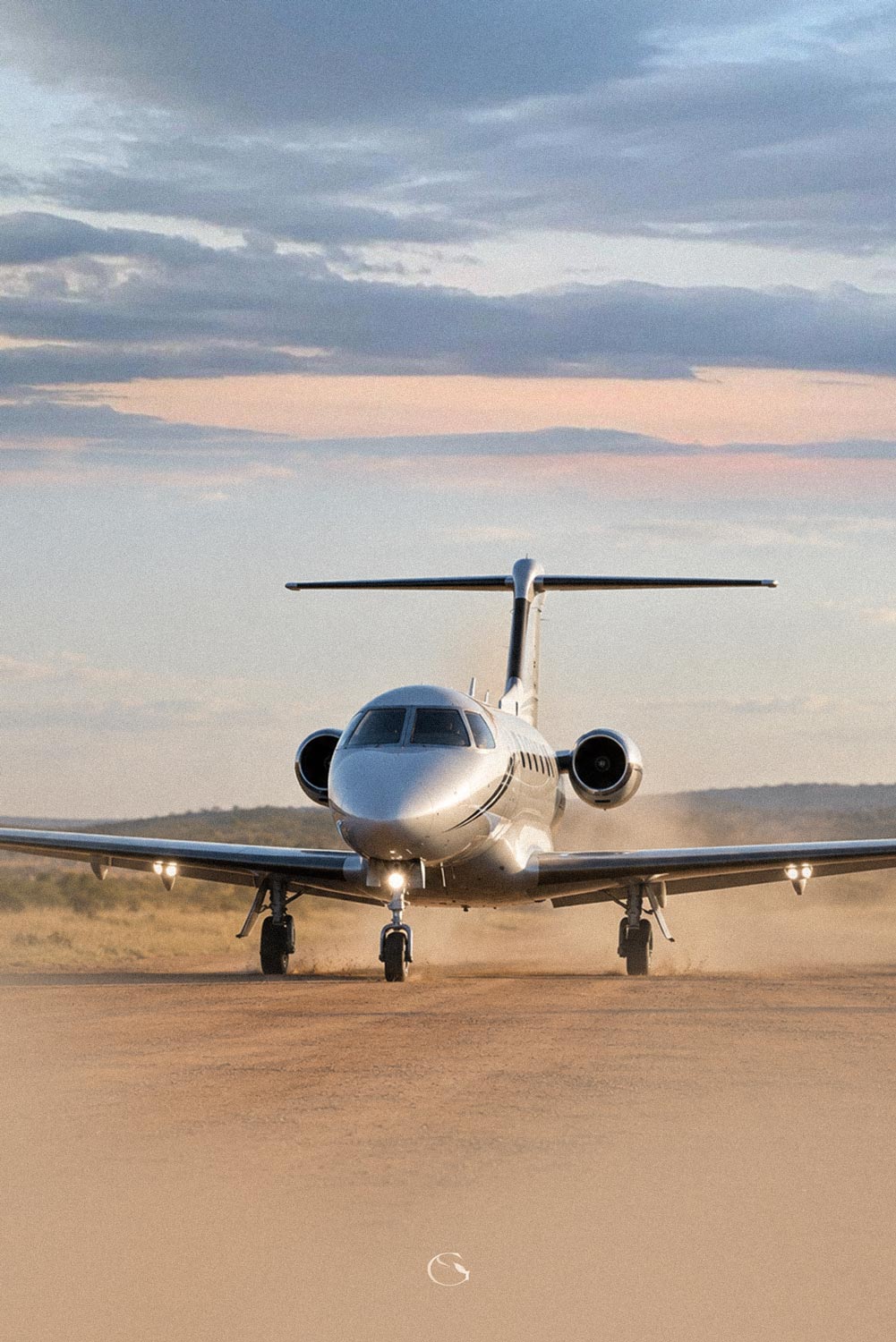 A private jet taxiing along a dusty bush airstrip at dusk